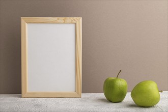 White wooden frame mockup with green apple on beige paper background. Blank, vertical orientation,