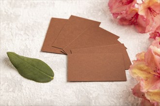 Brown business card with pink azalea flowers on gray concrete background. side view, copy space,