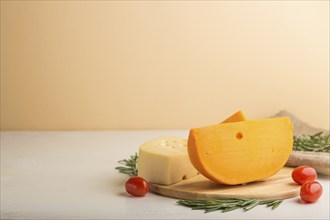 Various types of cheese with rosemary and tomatoes on wooden board on a white and orange background