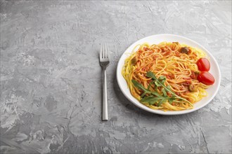 Corn noodles with tomato sauce and arugula on a gray concrete background. Side view, close up, copy