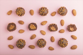 Chocolate caramel ball candies with almonds in a row on a pastel pink background. top view, flat