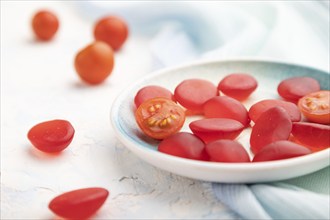 Jelly tomato candies on white concrete background and blue linen textile. close up, side view,