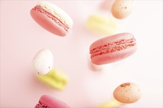 Multicolored flying macaroons and chocolate eggs frozen in the air on blurred pink background. top