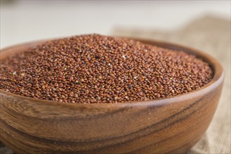 Wooden bowl with raw red quinoa seeds on a white wooden background and linen textile. Side view,