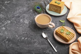 Homemade honey cake with milk cream and mint with cup of coffee on a black concrete background and