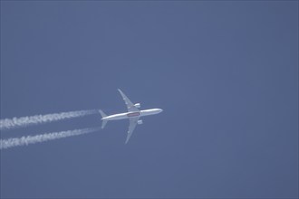 Boeing 777 aircraft of Emirates airlines flying across a blue sky leaving a contrail or vapor trail