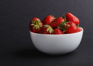 Fresh red strawberry in white bowl on black background. side view, close up