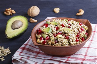 Salad of germinated buckwheat, avocado, walnut and pomegranate seeds in clay plate on black wooden