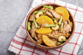 Fried pork with peaches, cashew and green beans in a wooden bowl on a gray concrete background. Top