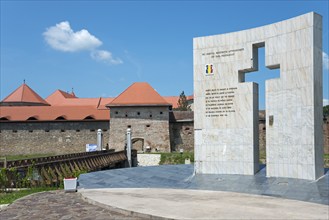 A modern monument with cross and inscription against the backdrop of an old fortress, Fortress and