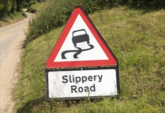 Red triangle road sign warning of Slippery Road, Suffolk, England, UK