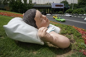 Cars on the city motorway in Tehran drive past the art object Sleeping Child. The city of Tehran is