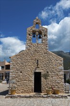 A traditional stone church with a bell tower under a clear blue sky and mountains in the