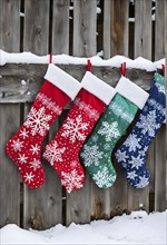 Row of Christmas stockings hanging from a snow-covered wooden fence, with delicate frost patterns