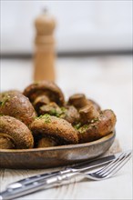 A wooden plate displays a heap of freshly cooked mushrooms seasoned with herbs, accompanied by a