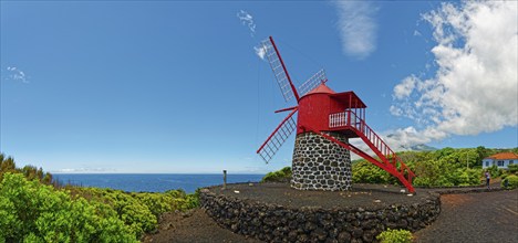 Red painted windmill on black volcanic stone Moinho de São João under a wide sky, São João, Pico