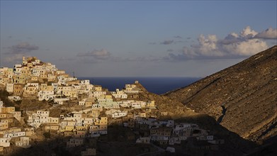 A mountain village with white houses illuminated by the rising sun while the background reveals the