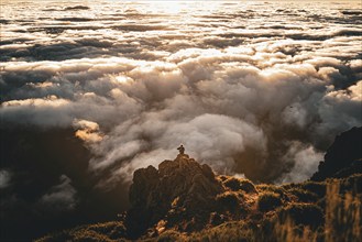 Person sitting on a rock looking over a cloud cover in the golden light of sunset, Pico Ruivo,