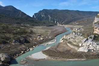 A clear jade river flows through a wide valley, surrounded by dramatic cliffs and wooded mountains