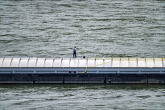 Inland waterway vessel, freighter, with closed cargo hatches, employee cleans the deck with water