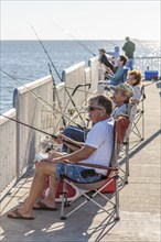 Adult men and women sitting and fishing from the fishing pier in the Gulf of Mexico at Cedar Key,