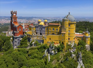 Magnificent castle with colourful towers and buildings in a green, hilly landscape under a blue