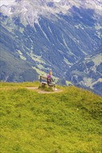 A woman sits on a bench and observes the sweeping valleys and green hills, Penken, Zillertal,