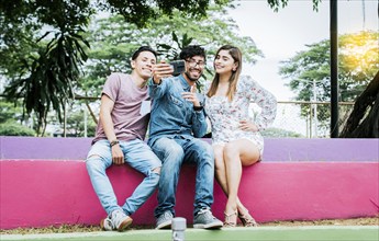 Lifestyle of three friends sitting in a park taking a selfie, Three teenage friends sitting in a