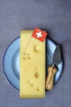 A piece of Swiss Emmental cheese on a plate and the Swiss flag