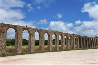 Historic aqueduct with stone arches in front of a blue sky with clouds, Aqueduto de Usseira,