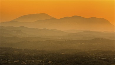 View from Filerimos hill in southwest direction, mountains in orange light at dusk, foggy