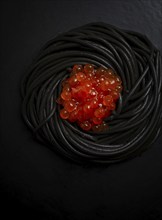 Black spaghetti with red caviar, pasta, on a black background, top view, no people