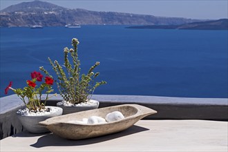 View of the sea and island, decorated with white stones and red flowers in pots, Santorini,