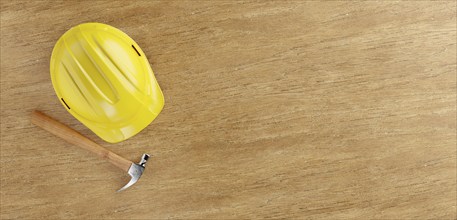 Overhead of yellow hard hat and hammer on a wood surface with room for text