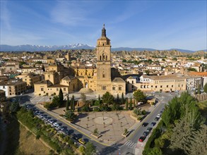 Historic town with a large church in the centre, surrounded by mountains and sunny skies. Trees and