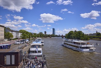 Excursion boats at the Main quay and on the Main river under a blue sky with cumulus clouds in