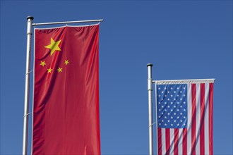 Chinese and American flags fly in front of a clear blue sky