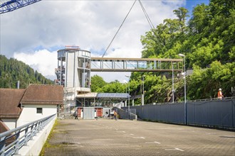 A bridge spanning between a modern building and a mountain with lots of greenery, bridge lift