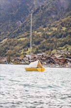 A yellow sailing boat rocks on the lake in front of a picturesque village on the mountain, Lake