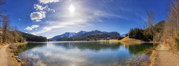 Clear mountain lake in quiet, sunny surroundings with reflecting water surface and forest backdrop,