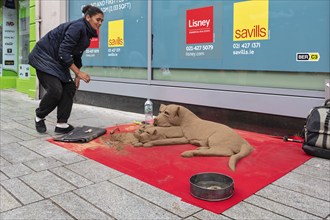 Street artist creates sand sculptures of dogs on a pavement, Cork