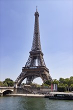 The Eiffel Tower next to a river and a stone bridge, captured on a clear summer day, Paris