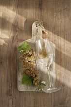 A sprig of white grapes, on a wooden board, with a glass of white wine, top view, natural lighting,