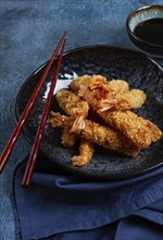 Shrimp in tempura, deep fried, on a black plate, with soy sauce, close-up, top view, no people