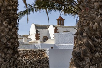 View of a church with traditional architecture through two palm trees, Canary Islands, Lanzarote,