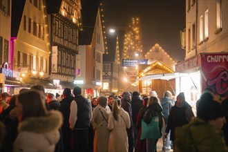 Full Christmas market at night with illuminated stalls and houses, surrounded by visitors,