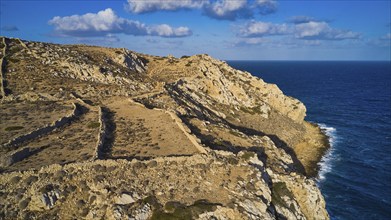 Drone shot, Archaeological site, Steep rocky coast above the blue sea, cloudy sky, Ruins of an