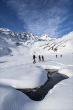 Small stream in a snow-covered mountain landscape, ski tourers in a valley, ascent to the