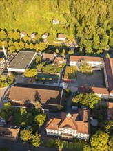 Aerial view of a neighbourhood with several buildings and lots of greenery, surrounded by trees and