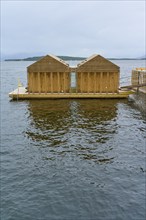 Outdoor sea pool by the fjord with small wooden sauna huts, overcast sky and calm water, Molde,